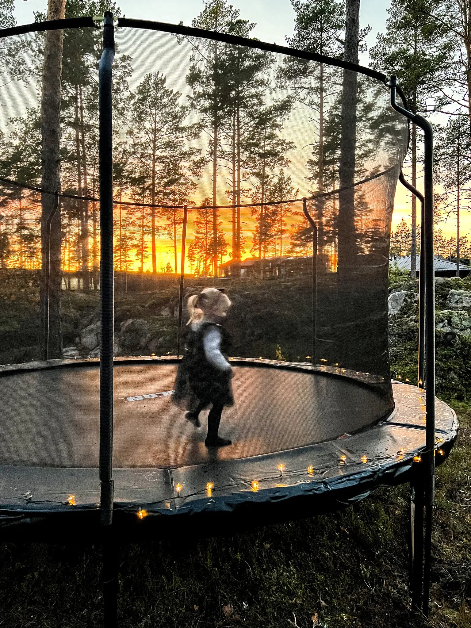 A little girl jumping on a round trampoline with safety enclosure.