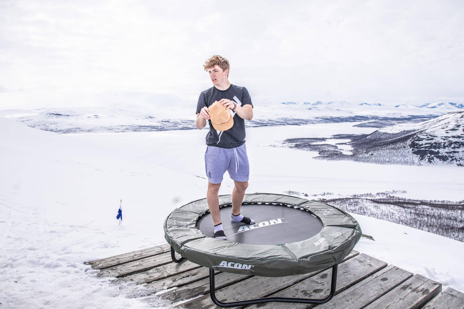 A guy standing on a mini trampoline in a Lapland landscape.