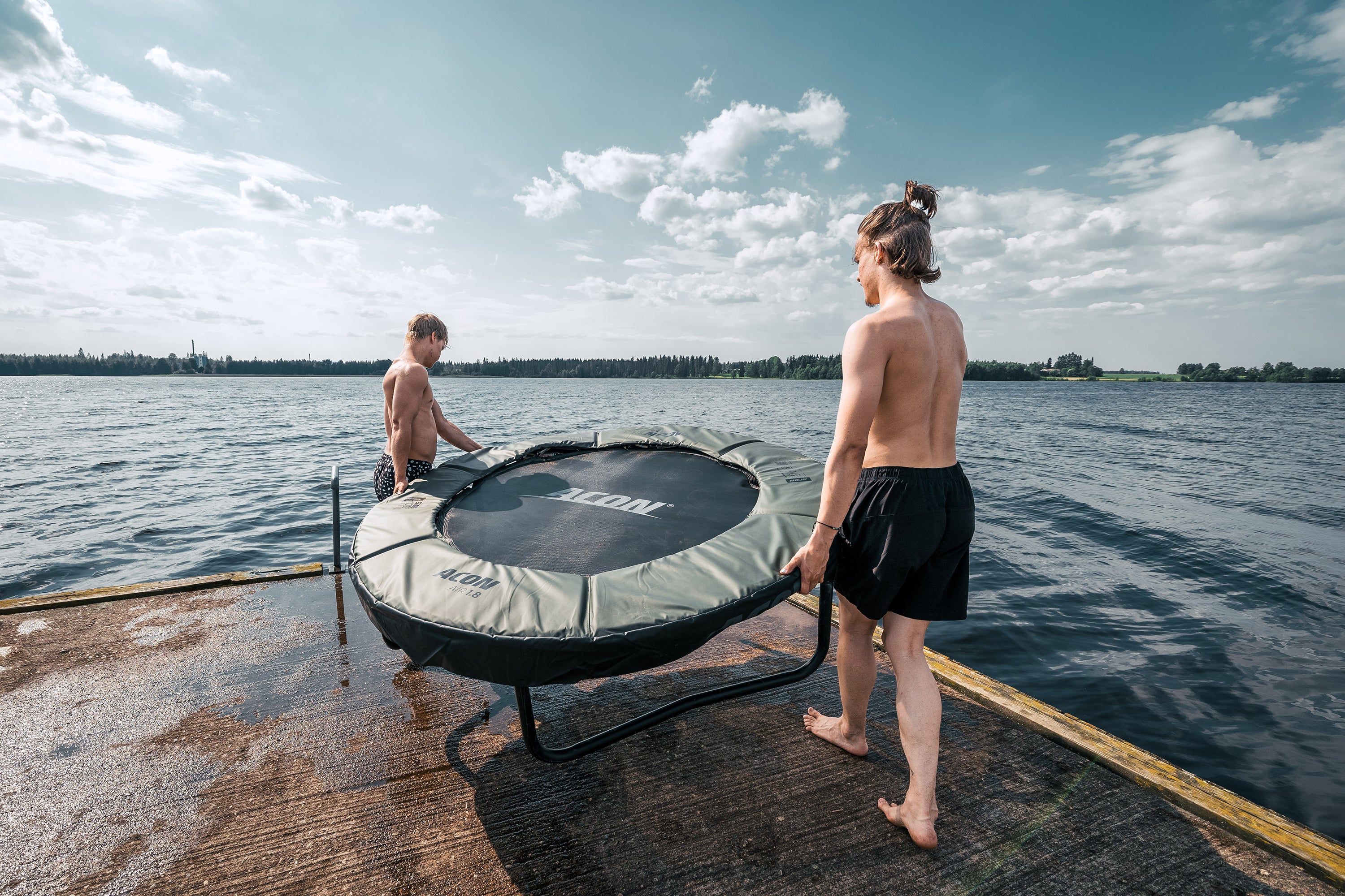 Two boys carrying a baby acon on a pier by a lake.