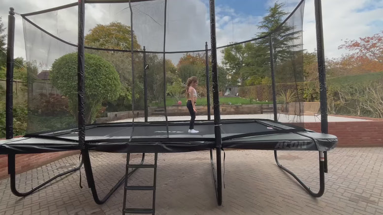 A young girl performs flips and cartwheels on an Acon 16HD trampoline outdoors in bright daylight.