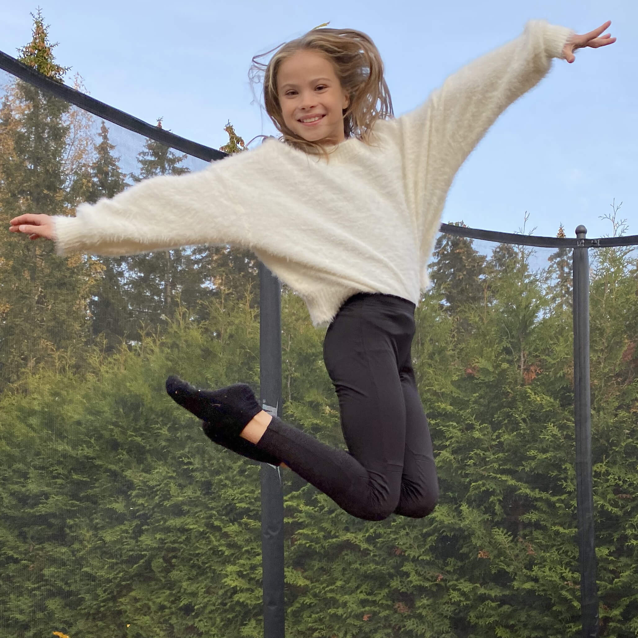 A smiling girl jumping on an Acon trampoline with safety net
