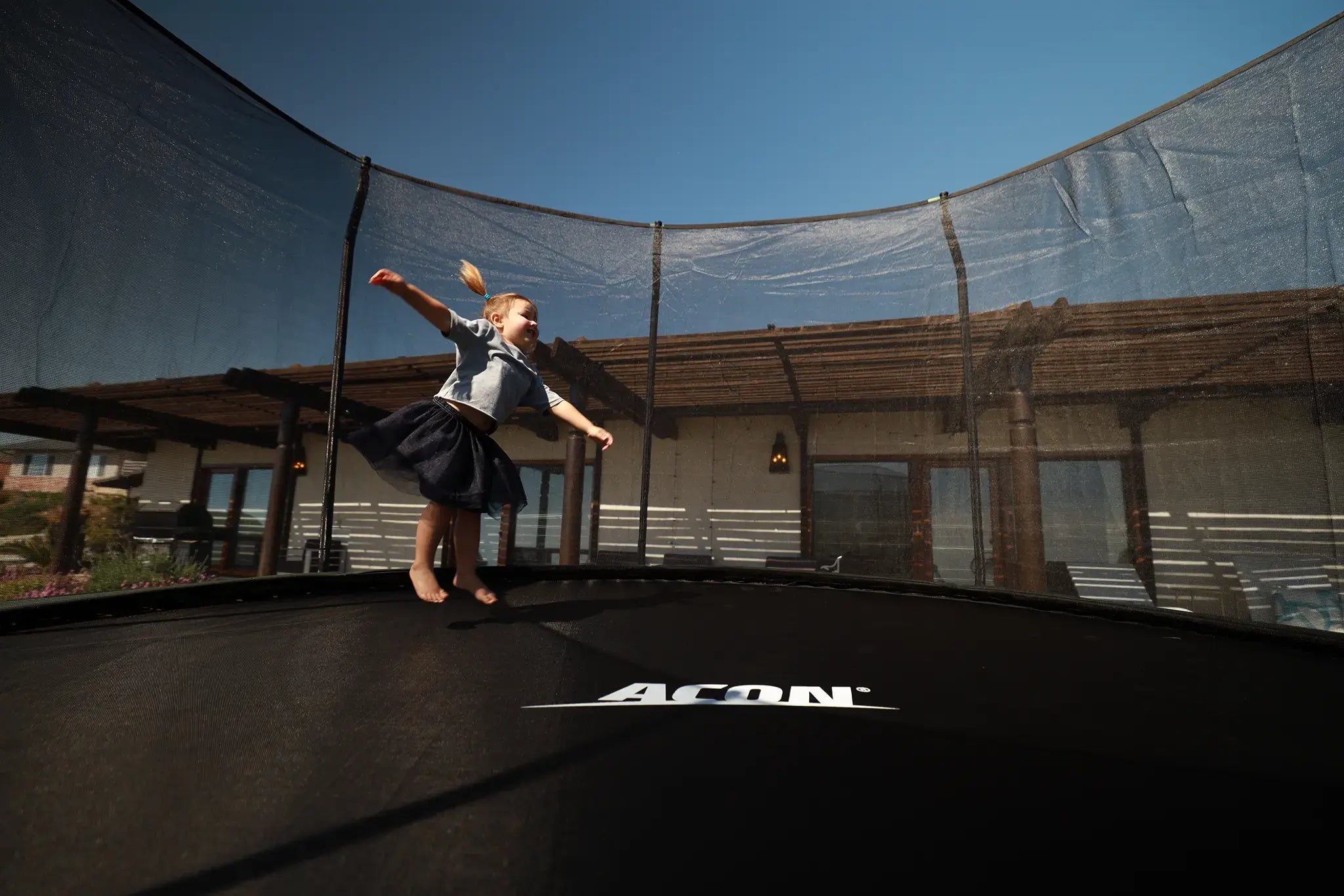 Young toddler jumping on a round Acon trampoline with safety net. 
