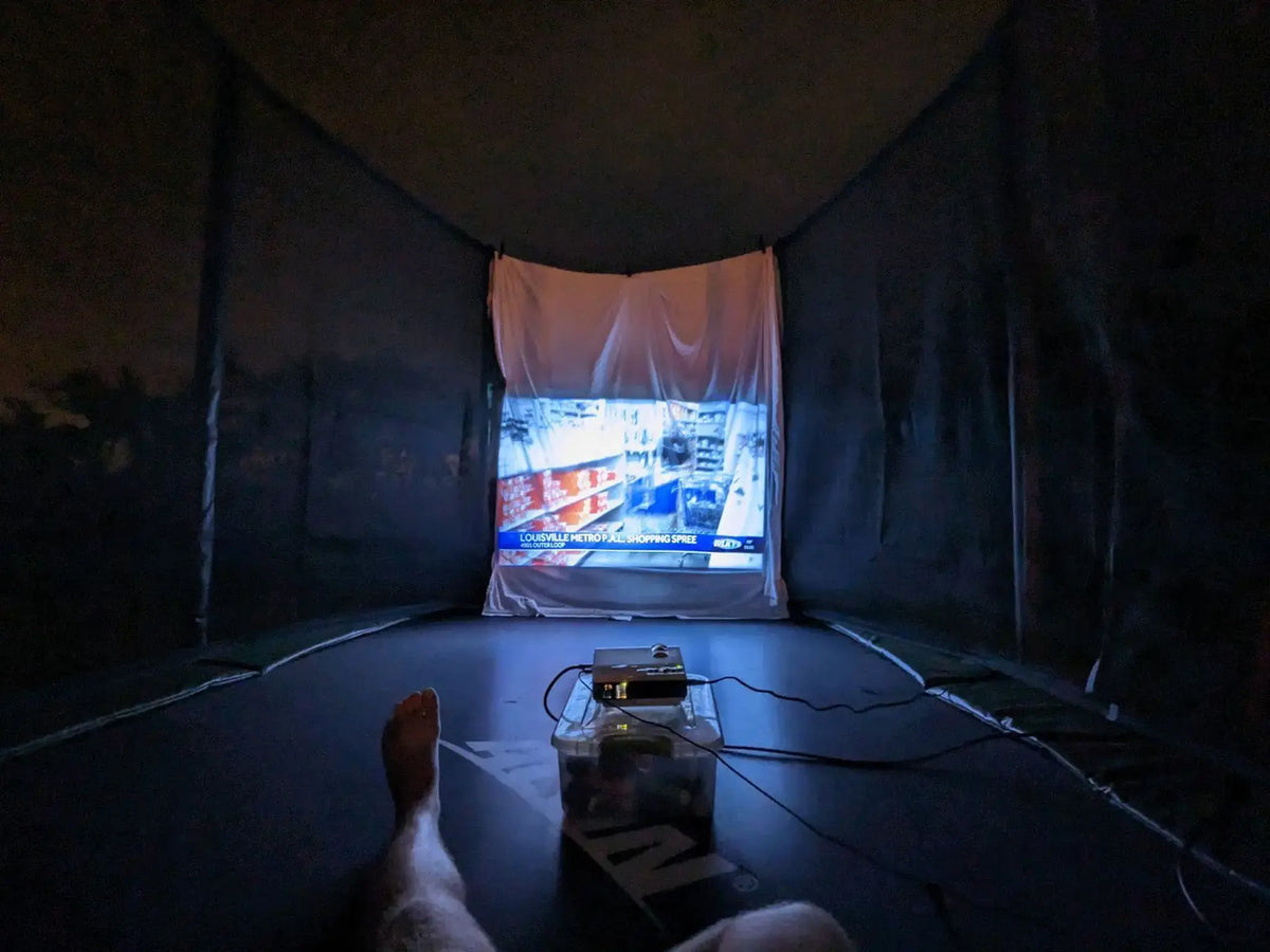 Projector displaying a movie on a white screen inside a trampoline enclosure.