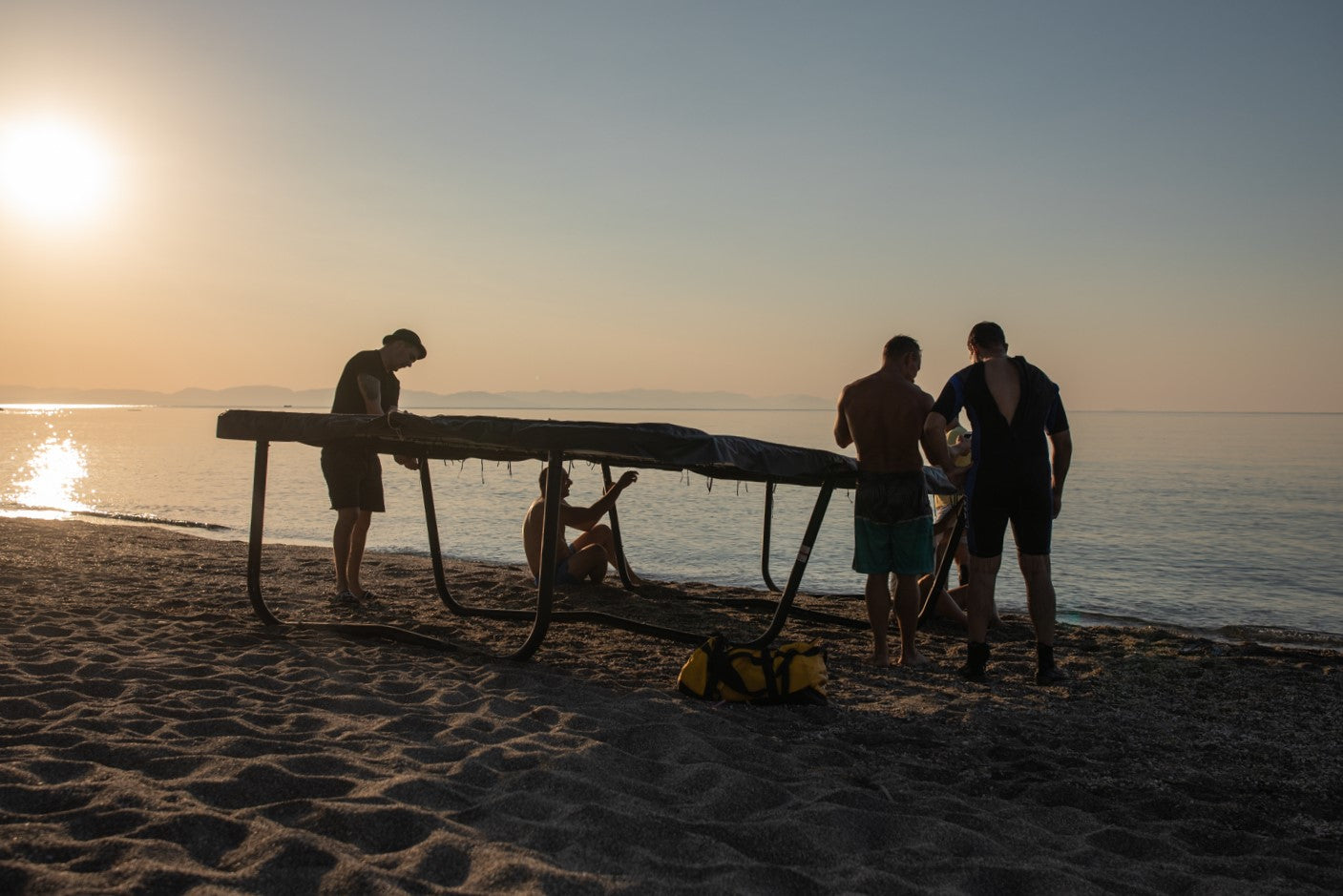 Guys hanging around next to a trampoline after tricking session on a beach