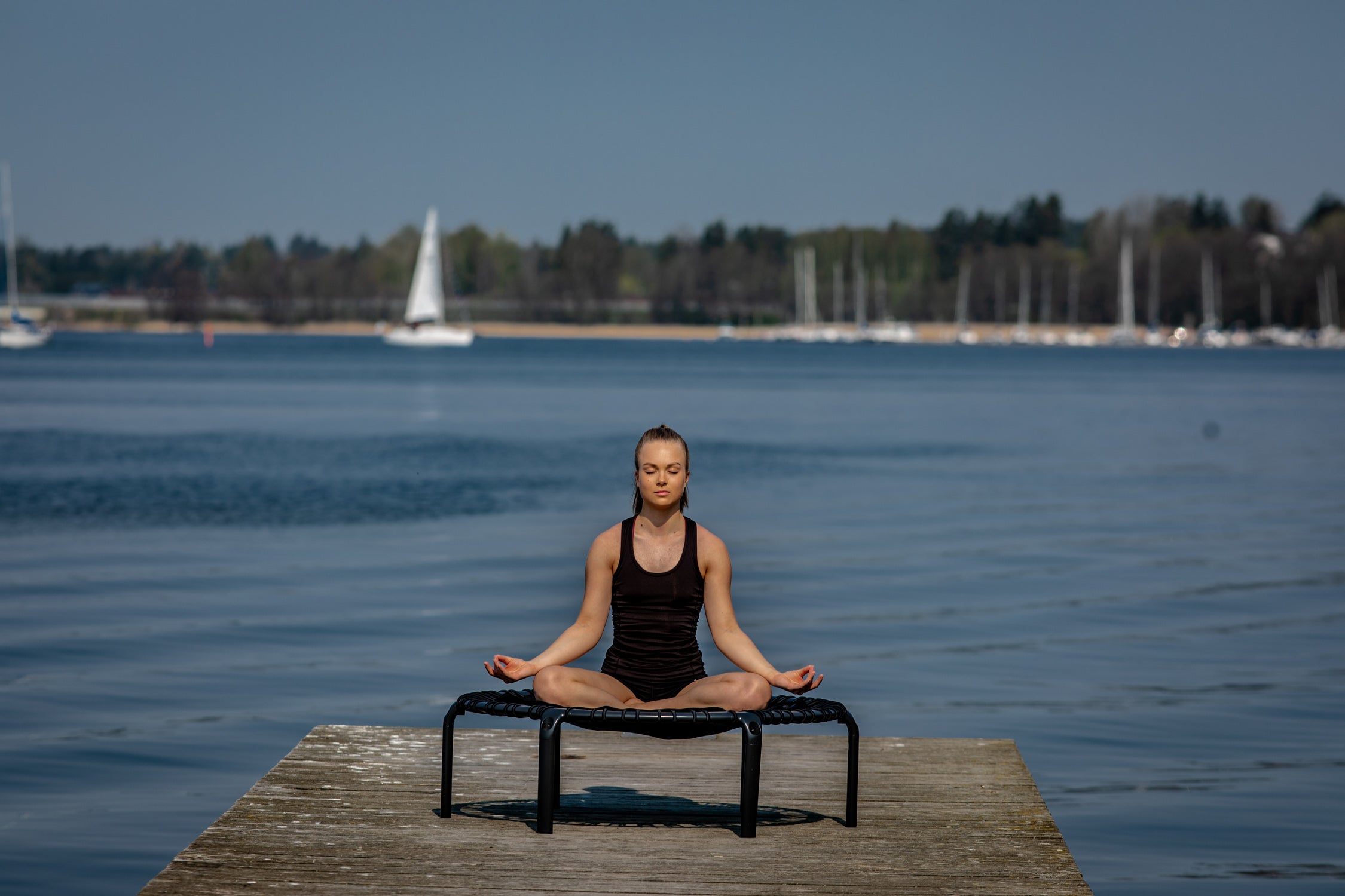 A young woman meditating and sitting on top of a rebounder trampoline