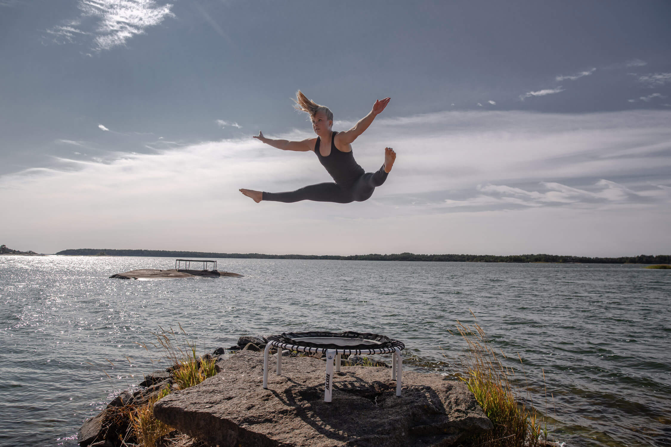 A woman jumping high on a fit rebounder in an archipelago lanscape.