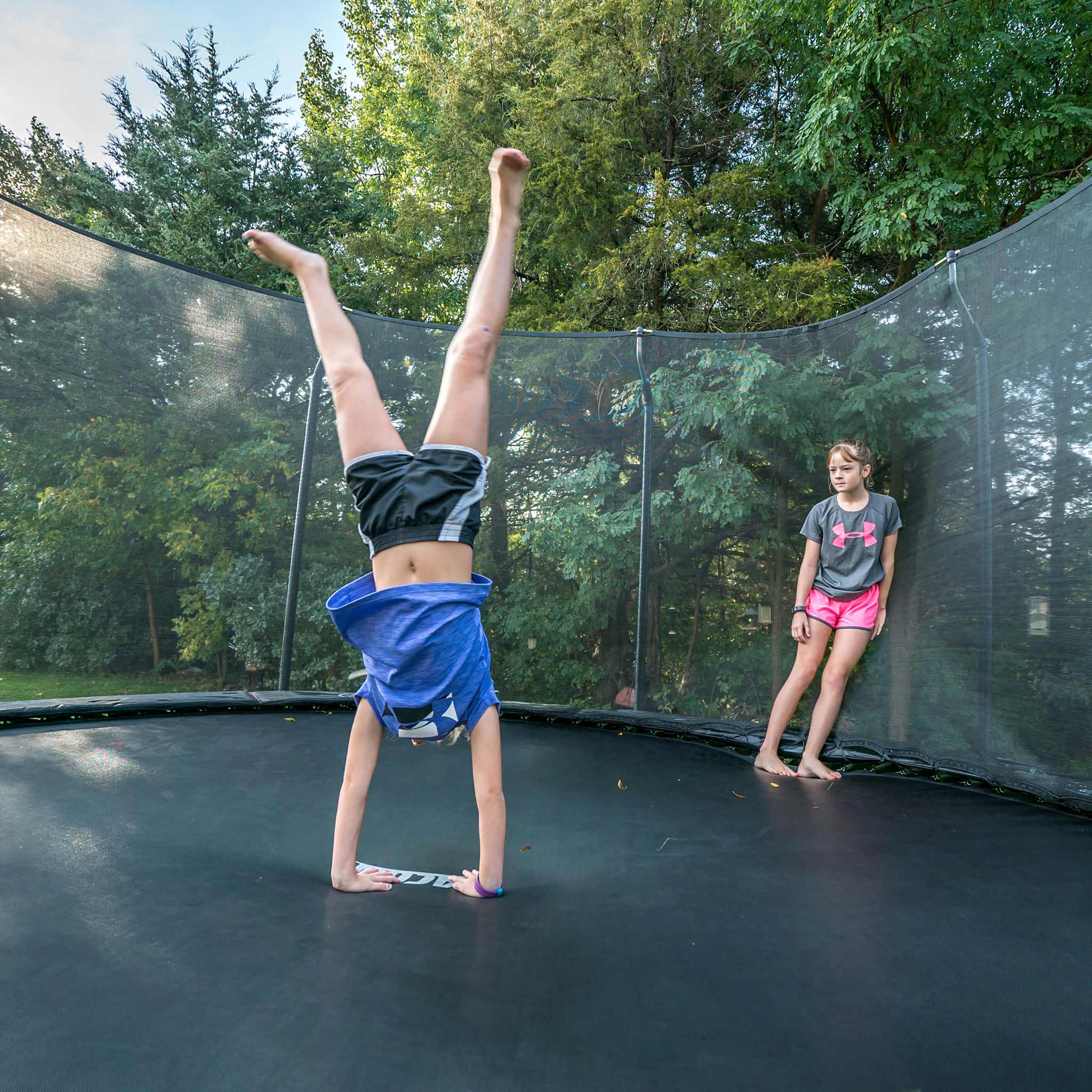 A girl handstands on an Acon trampoline, a friend watching.