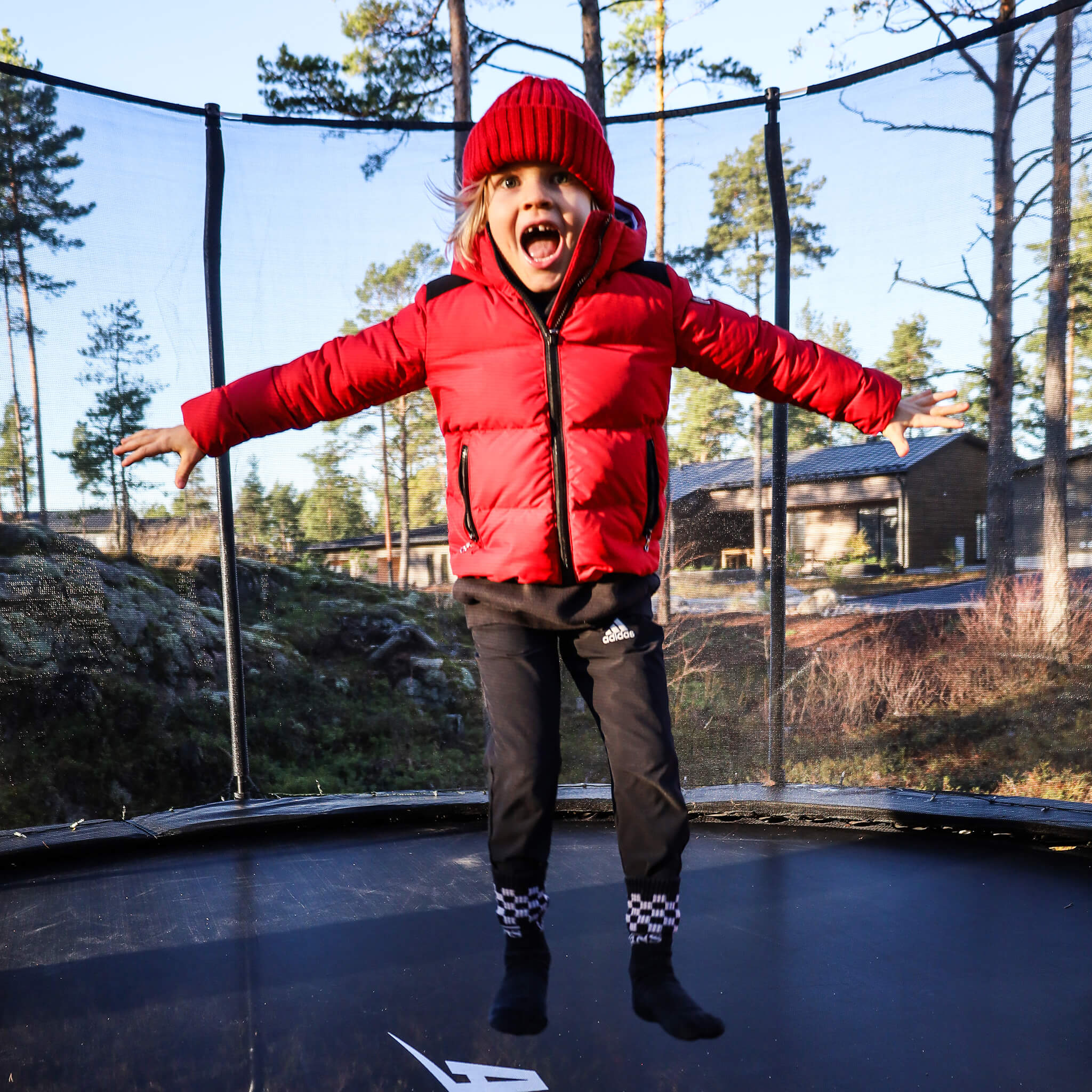 A girl in a red jacket jumps on an Acon trampoline.
