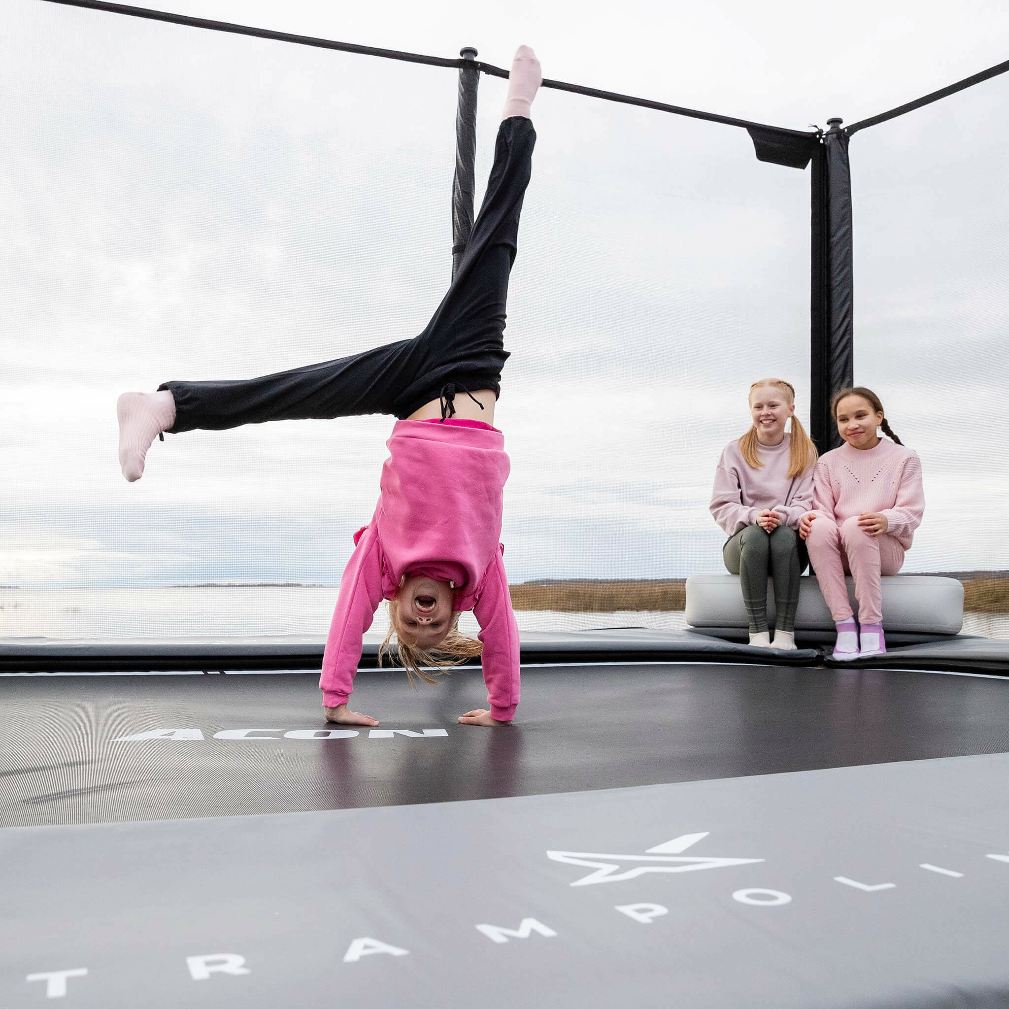 Two girls sitting on the Acon X Inflatable Triangle Block. The girl stands with her hands on the trampoline.